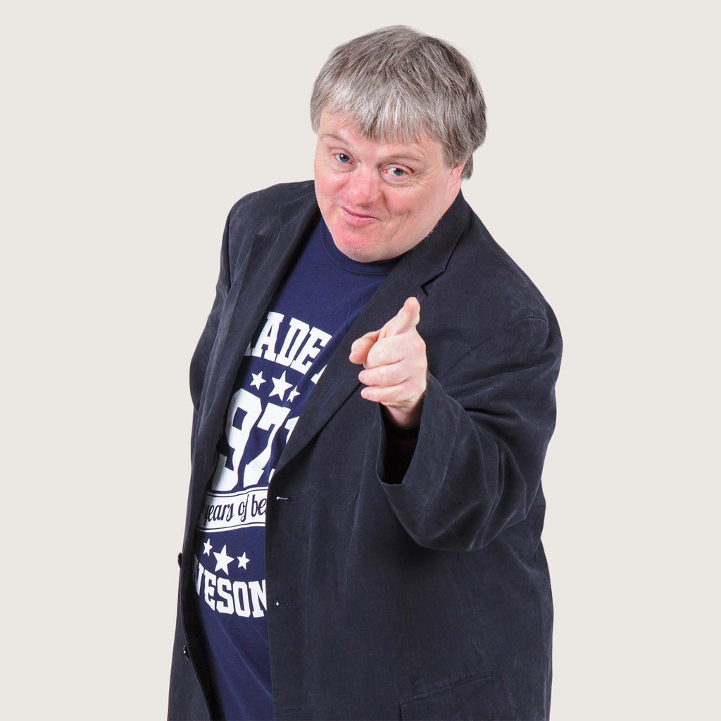 Benedict - A middle aged white man with Downs syndrome. He is wearing a suit jacket and T-shirt and is pointing at the camera.