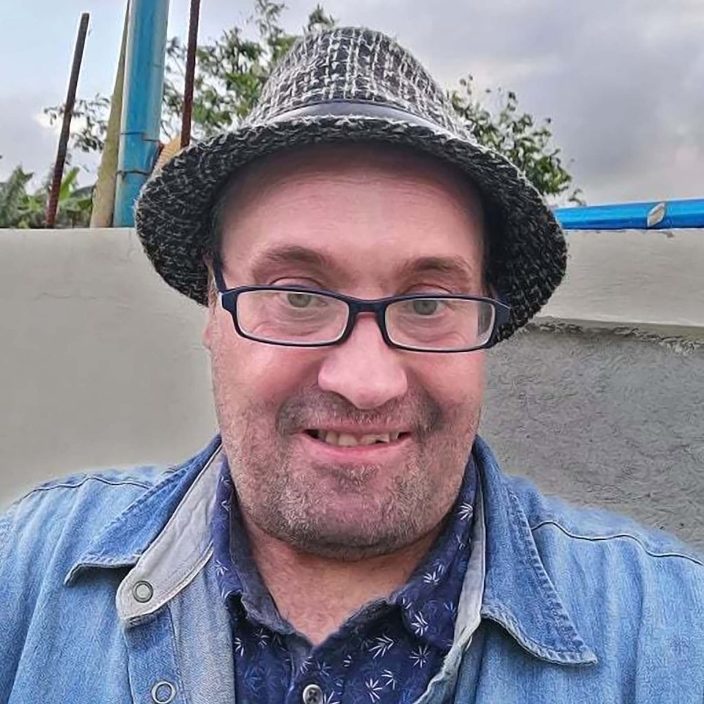 A headshot of Shaun out and about - he is wearing a trilby hat and summer shirt with a denim jacket.