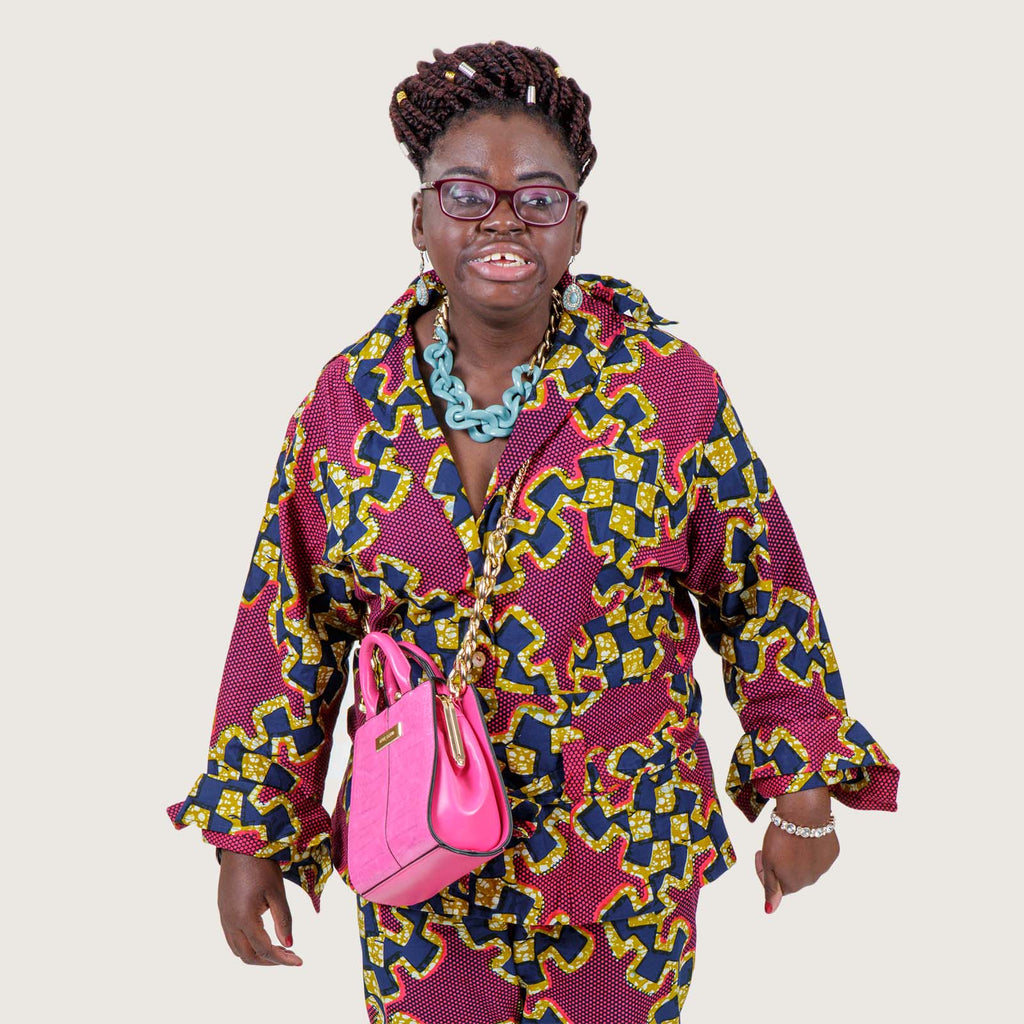 Sumaya - A young Black British woman with Downs syndrome wearing a colourful African outfit with bright pink handbag.