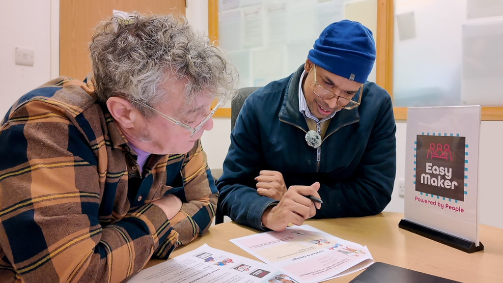 Pete from Photosymbols and Sanjay from Camden People First reviewing Easy Read documents with an EasyMaker sign on the table.
