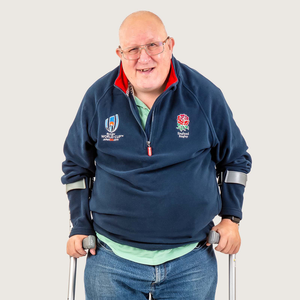 Bill - An older white man using sticks for support. He is wearing a fleece with a rugby logo.