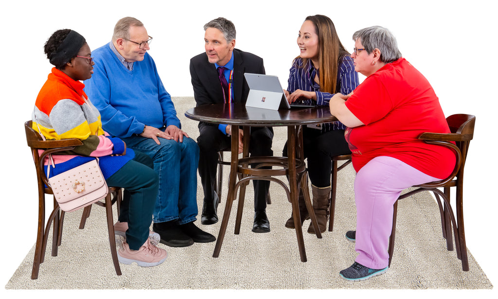 A group of people around a table are having a discussion, one person is making notes on a laptop.