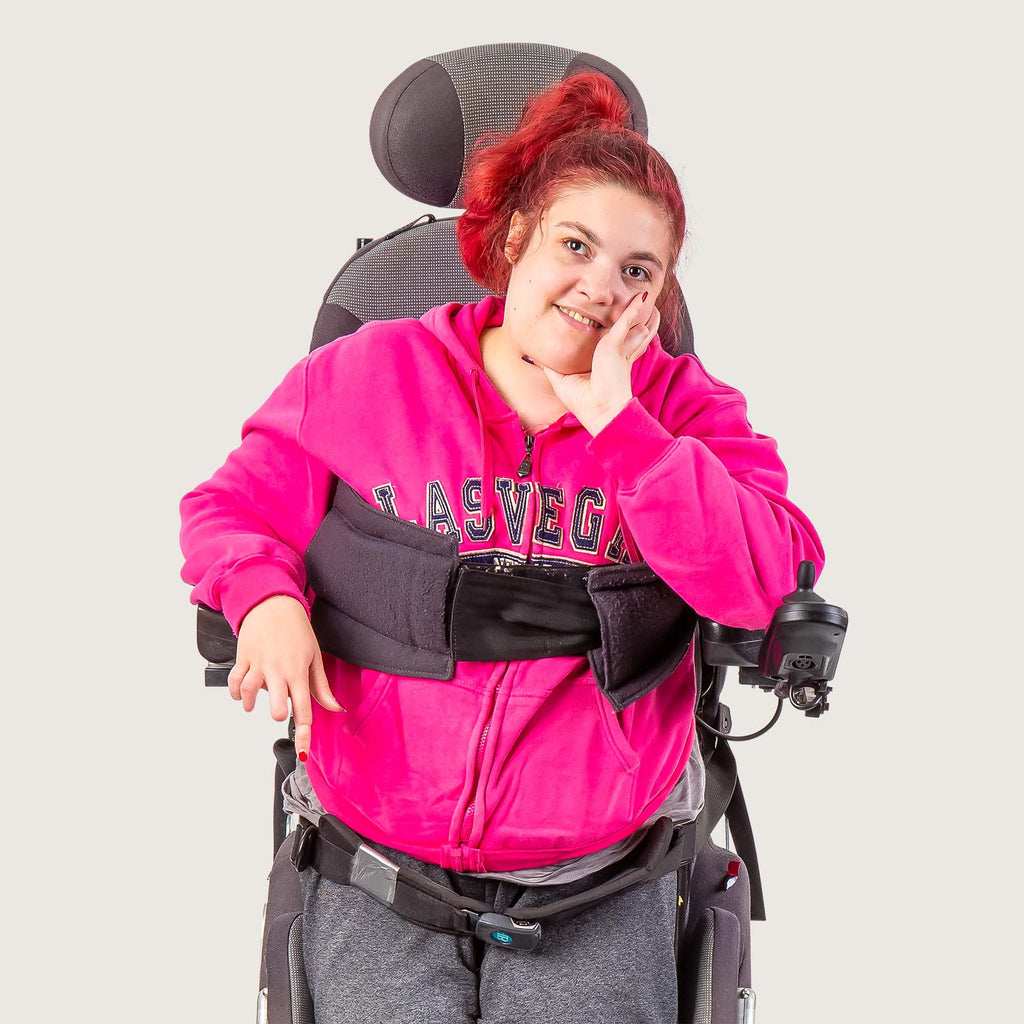 Clara - A young white disabled woman who uses a sitting-to-upright battery powered wheelchair. She wears bright pink and is looking thoughtful.
