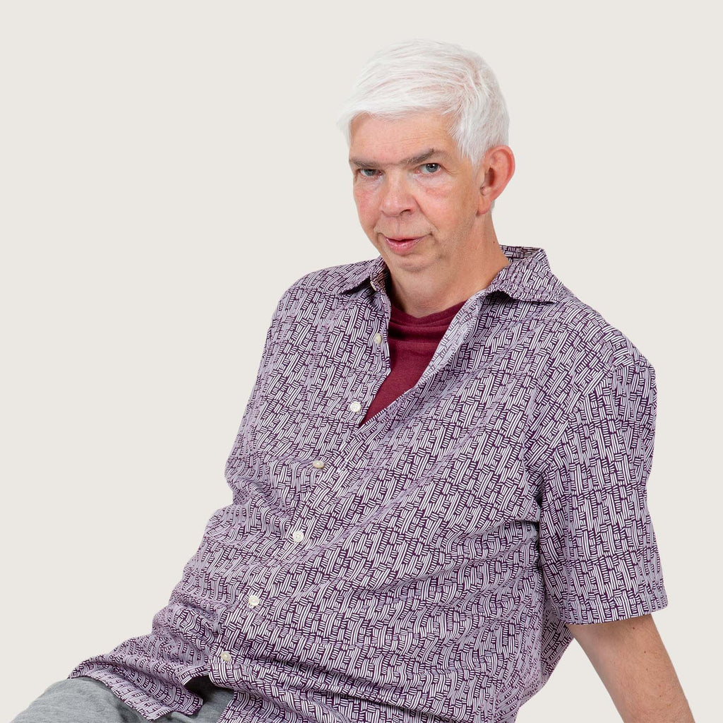 Mikey - An older white man with a shock of white hair. Mikey has Williams syndrome and wears a purpler summer shirt and shorts.