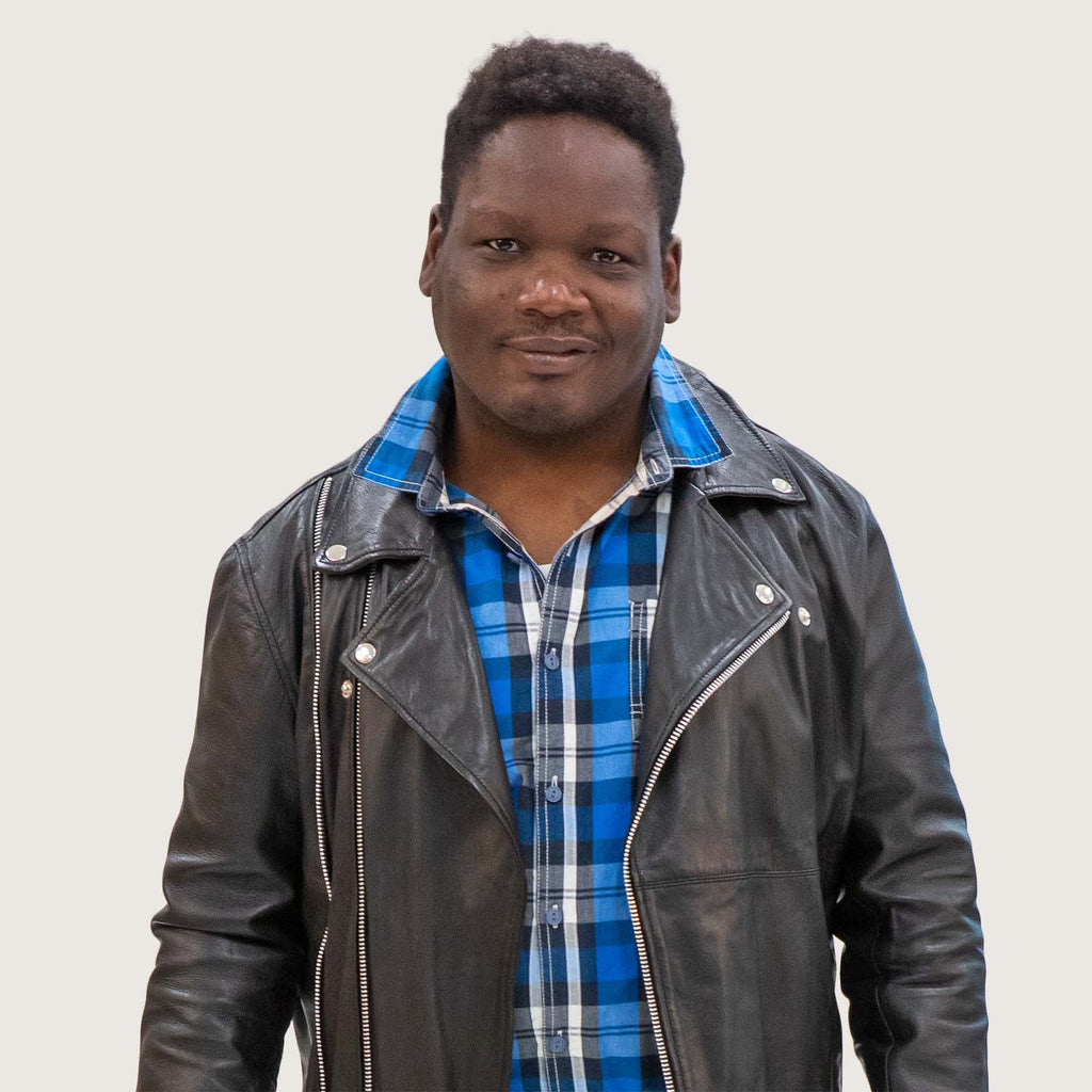 Mr Jostin - A young Black British man wearing a blue checked shirt and black leather biker jacket.