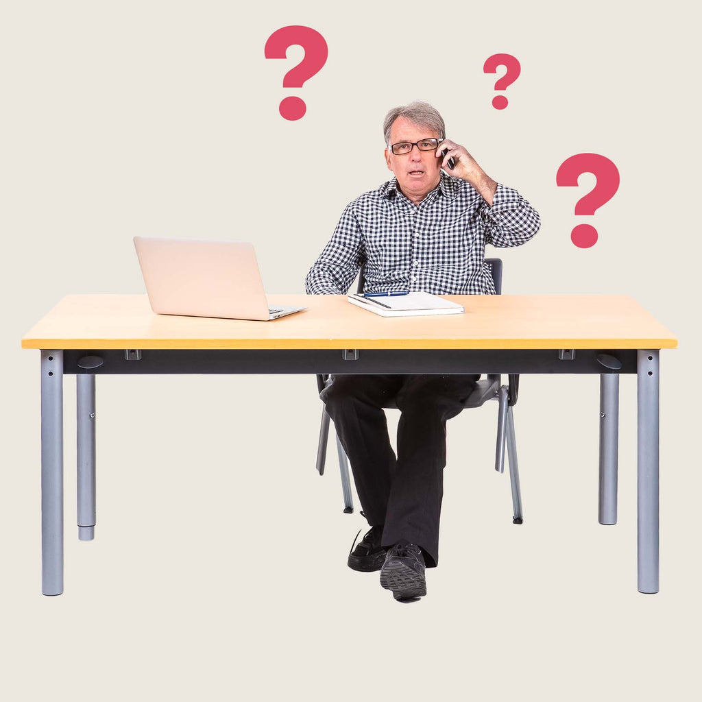 A man sat at a desk with a laptop and some papers. He is on the phone and looks confused. There are question marks as graphics around him.