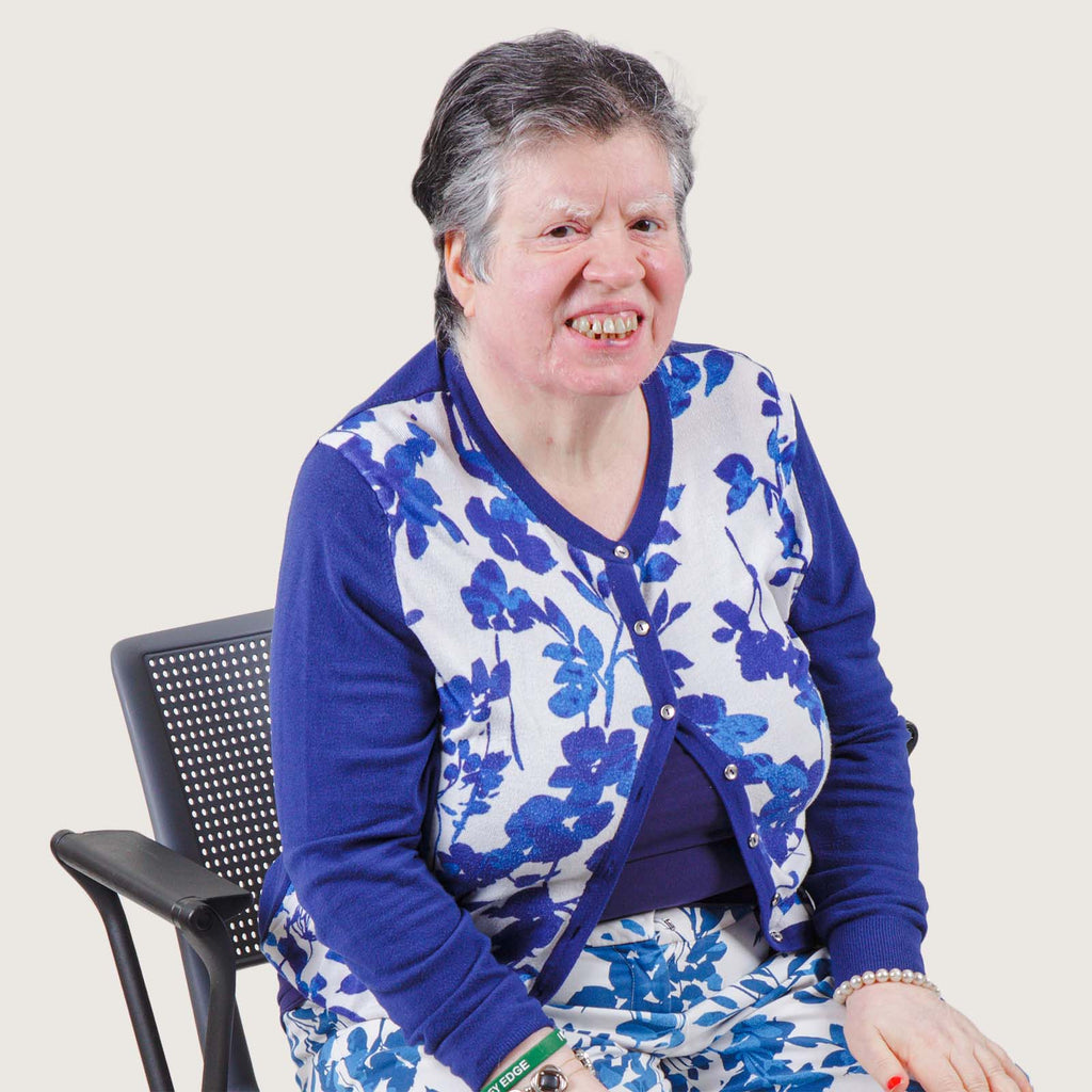 Sheila - An older white woman with short wavy hair wears a matching blue and white top and trousers.