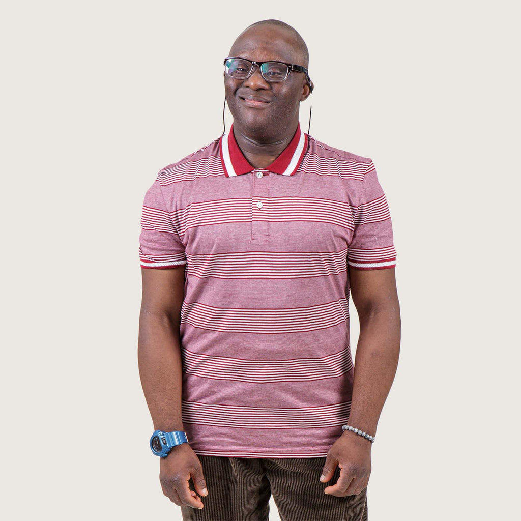 Wolu - A young Black British man with Downs syndrome. He has short cropped hair and glasses and wears a smart polo shirt and brown cords with a bright blue watch.