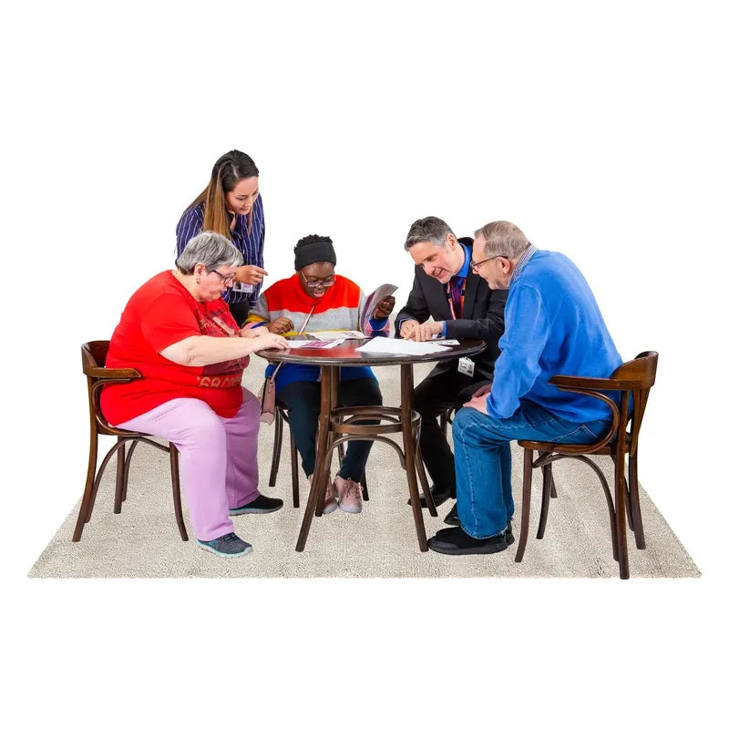 Five people round a table working on some papers together. One of them stands and leans in to help.