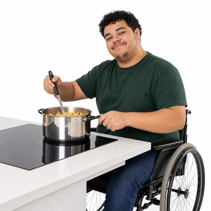The picture PictureMaker made: a smiling young man in a wheelchair stirring a pan of pasta on a hob at a low kitchen counter.