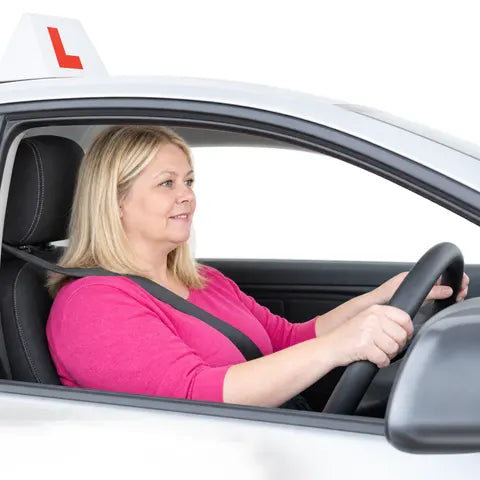 A woman with blonde hair driving a white car with an L plate on the roof.